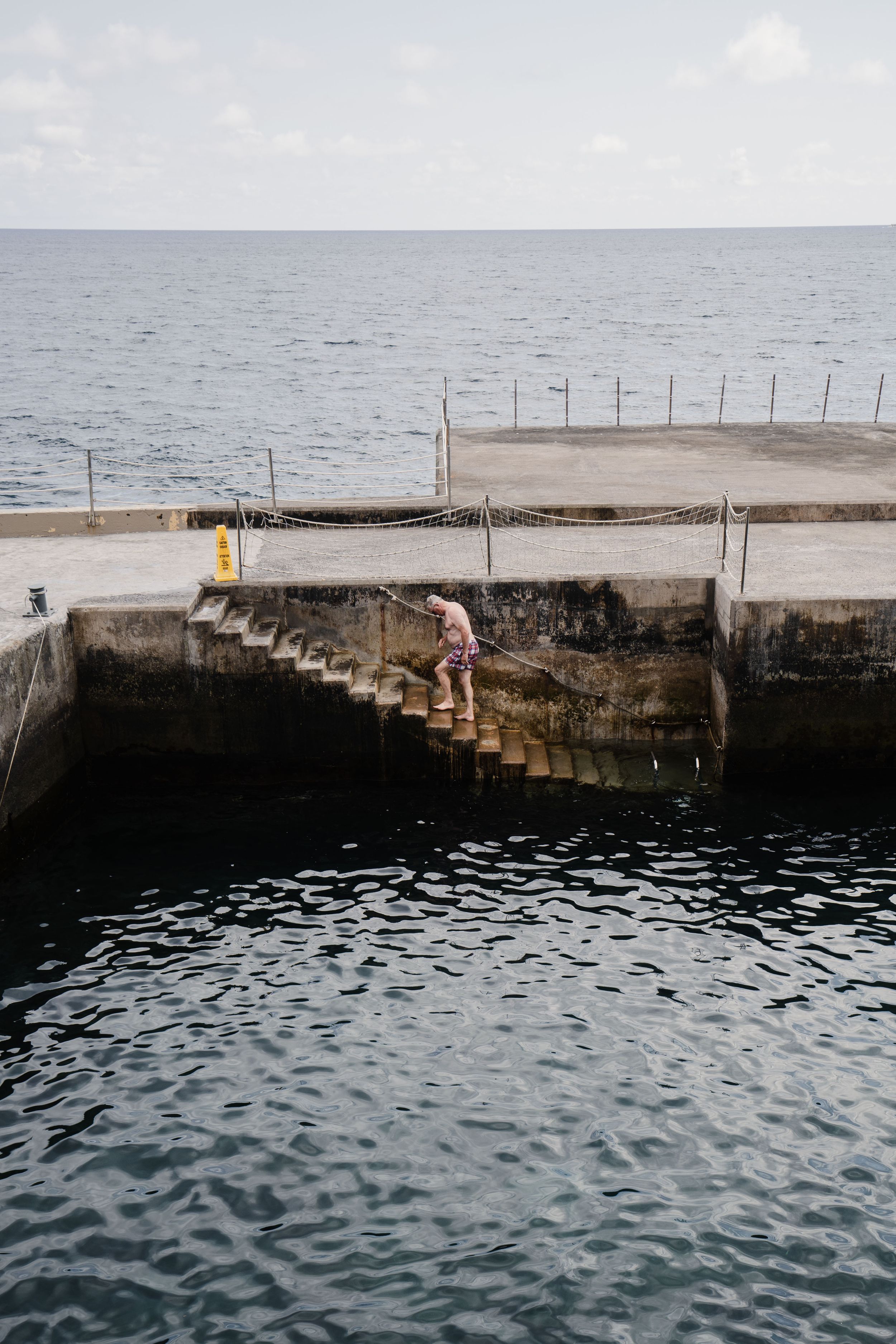 A concrete pier with steps leading down to dark ocean waters against a misty horizon.