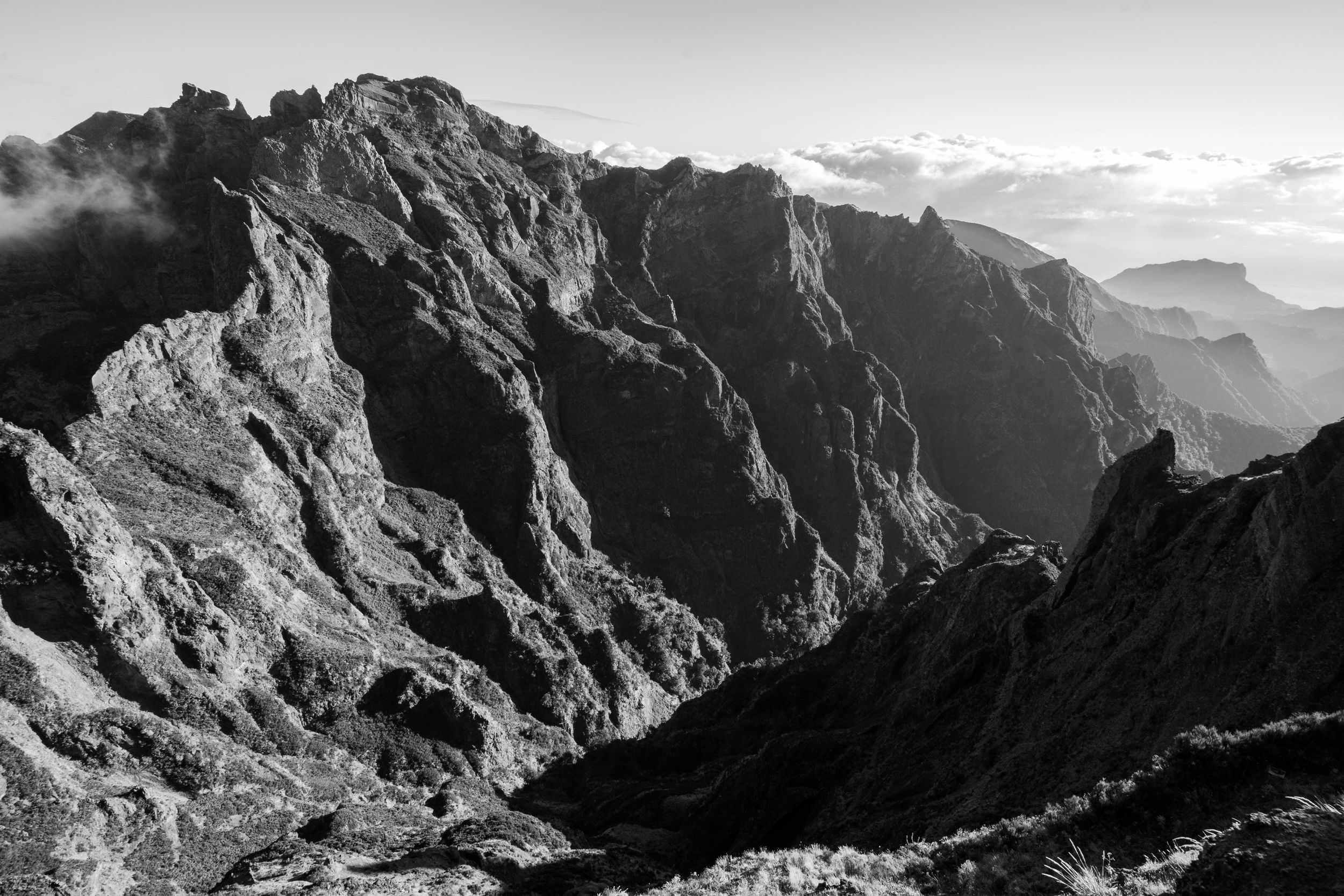 Dramatic black and white mountain landscape showing deep valleys and jagged peaks in harsh contrast.