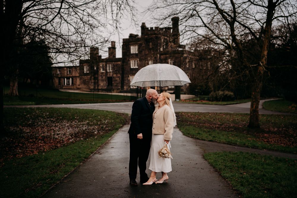 A couple walks along a tree-lined path holding a white umbrella on an overcast day.