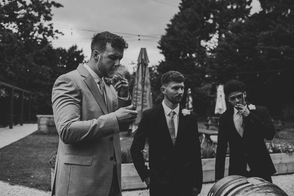 Black and white photo of groomsmen in suits sharing a moment outdoors at a wedding venue.
