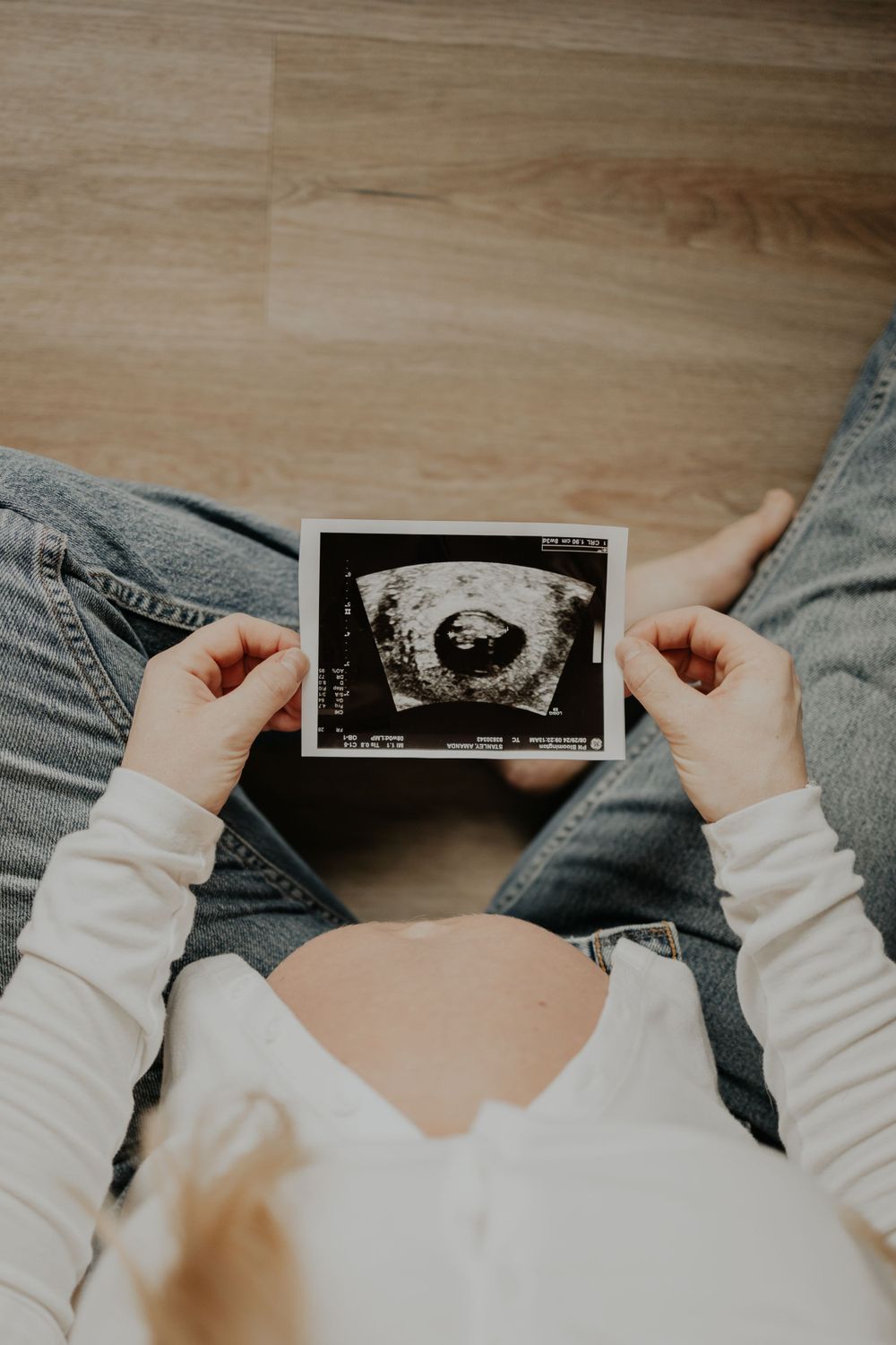 Overhead view of hands holding a sonogram ultrasound photo while sitting cross-legged on a floor.