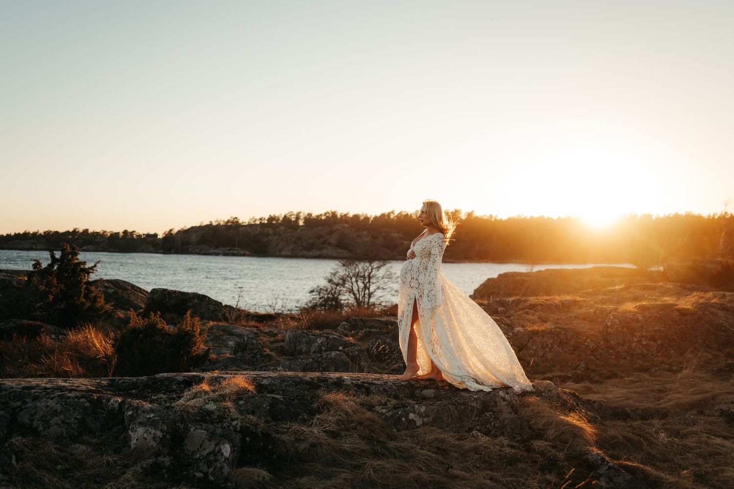 Gravidfotografering på en klippa i solnedgången i en vacker bohemisk klänning