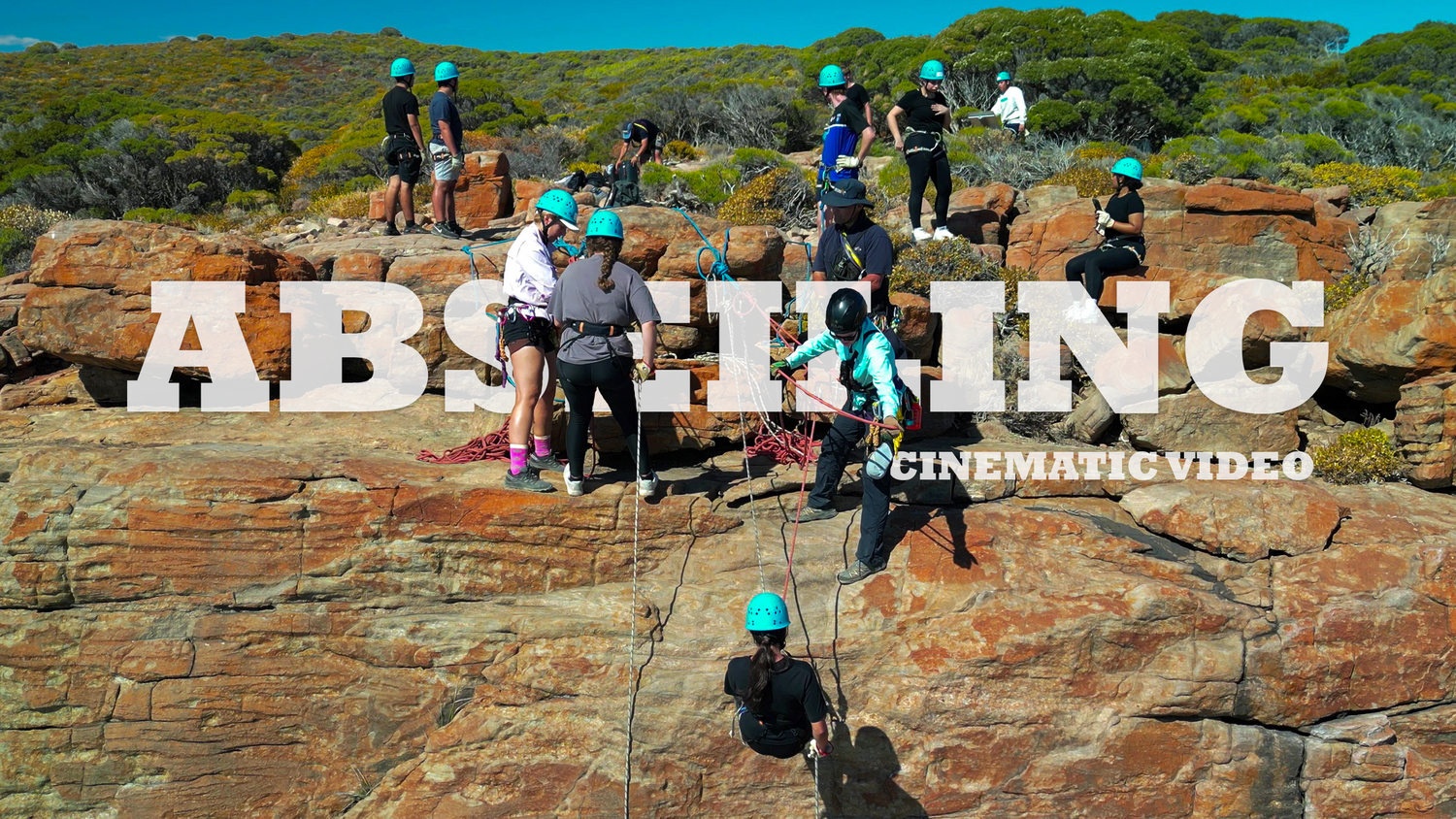 Group of hikers gathered around large rock formation letters spelling 'ABSEILING'.