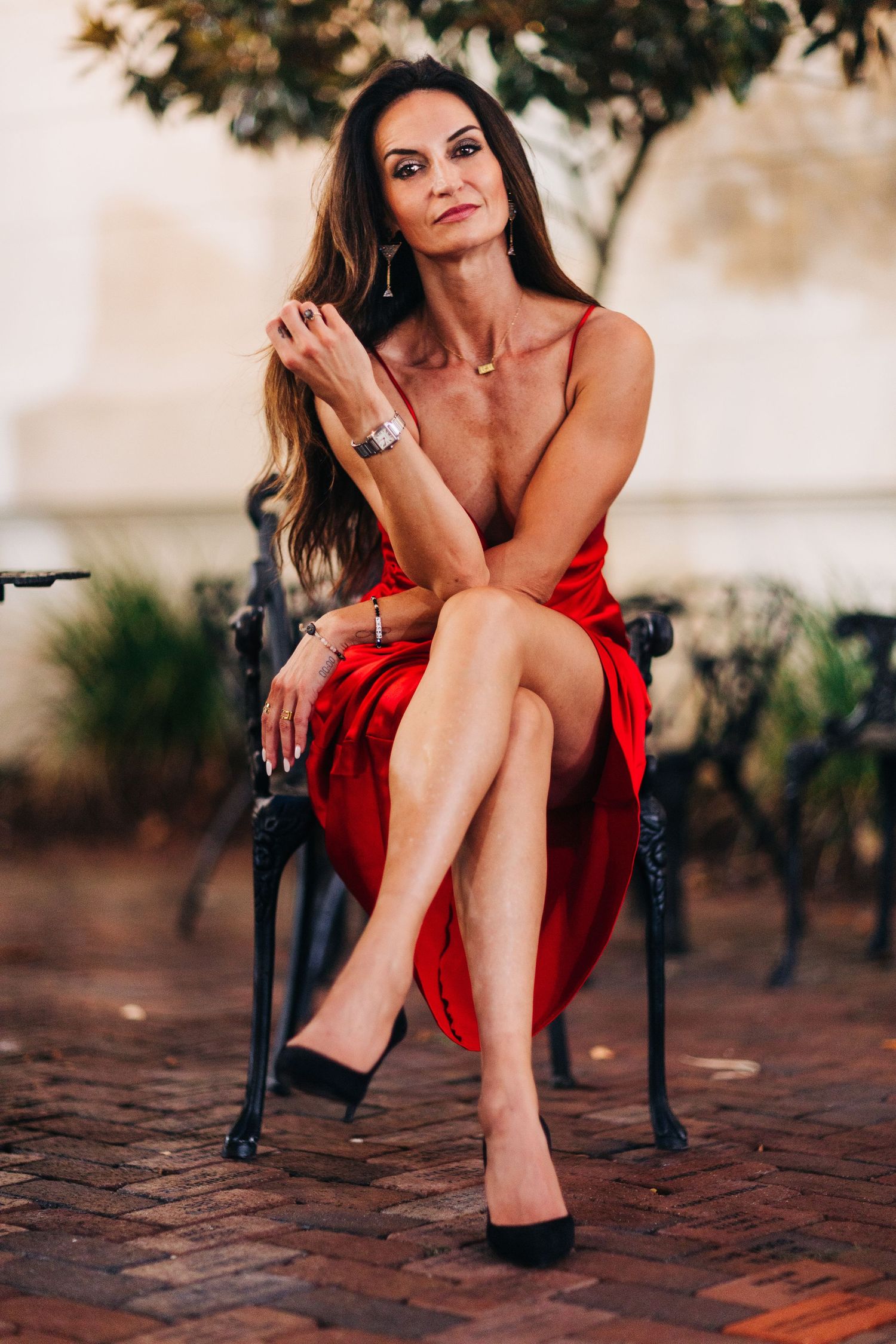 Woman in red dress poses gracefully on stone bench against blurred outdoor background.
