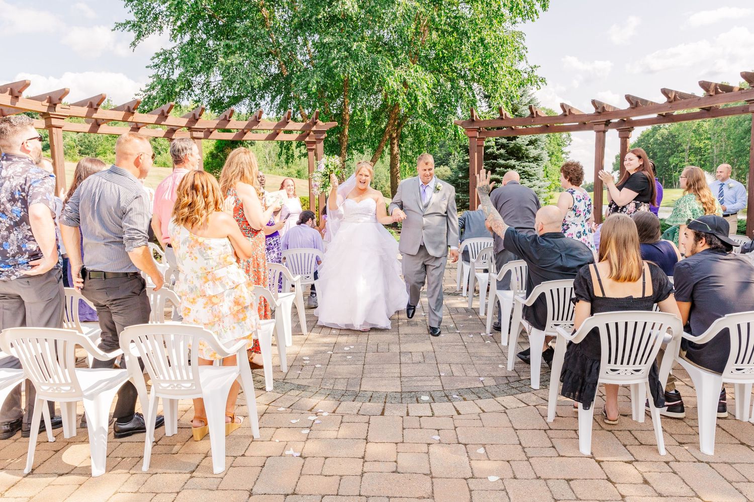 Wedding guests seated under wooden pergola during outdoor ceremony.