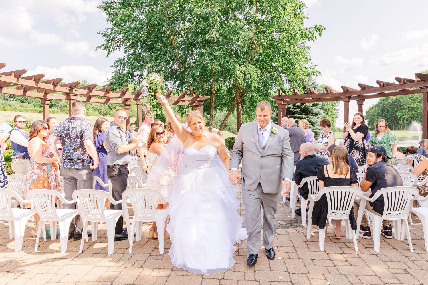 Wedding party and guests celebrating on brick patio under wooden pergola.