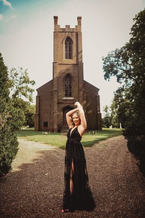 Gothic stone church with tower stands against blue sky on gravel path.