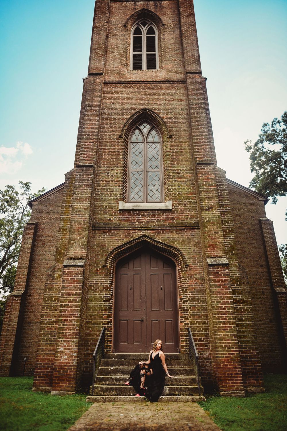 Gothic brick church with arched windows and wooden door serves as backdrop for dramatic portrait.