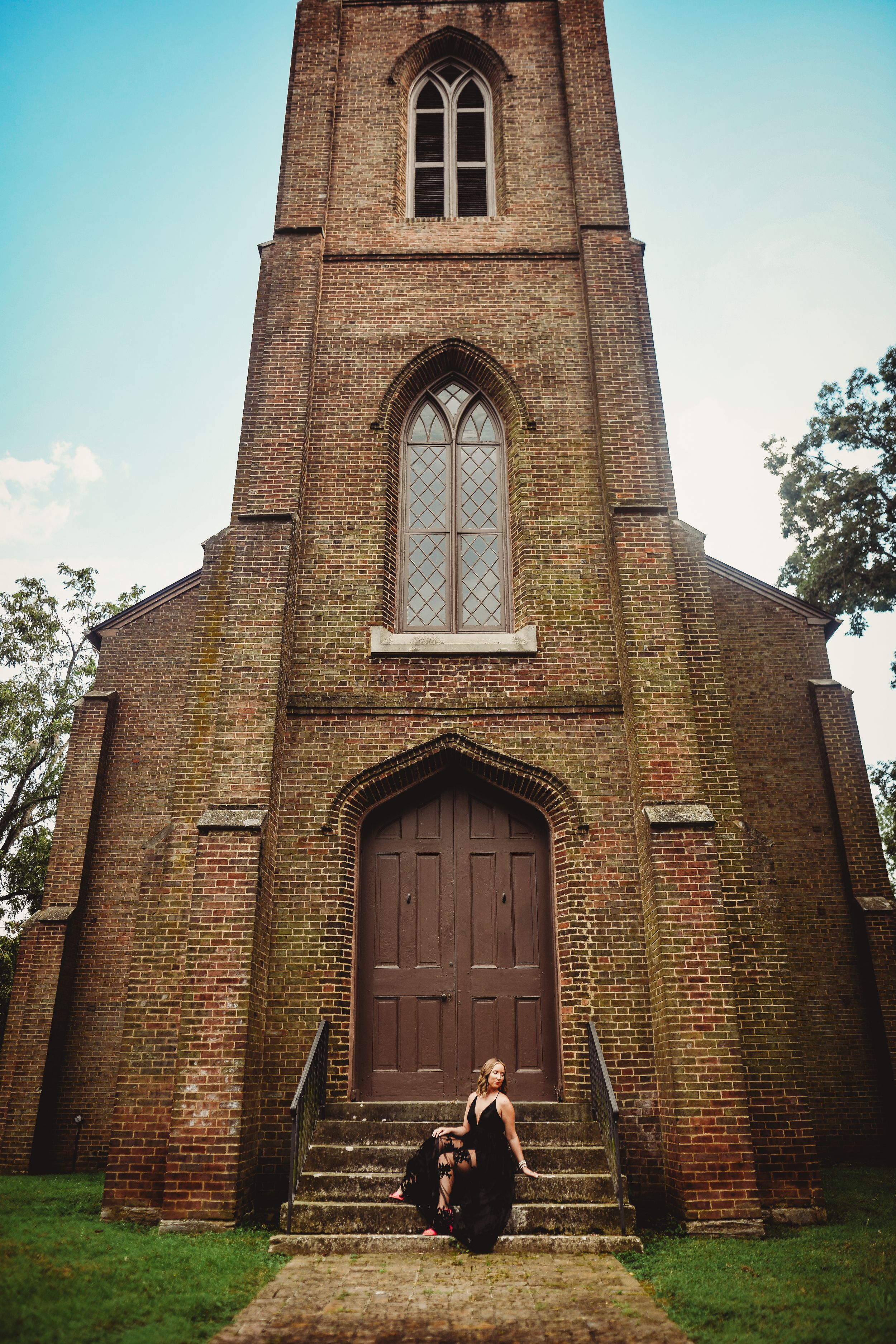 Gothic brick church with arched windows and wooden door serves as backdrop for dramatic portrait.