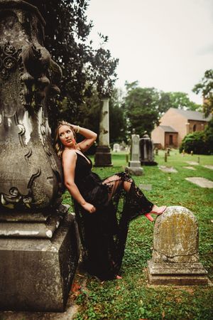 A dramatic fashion photoshoot among old cemetery monuments features a black lace dress against weathered stone.