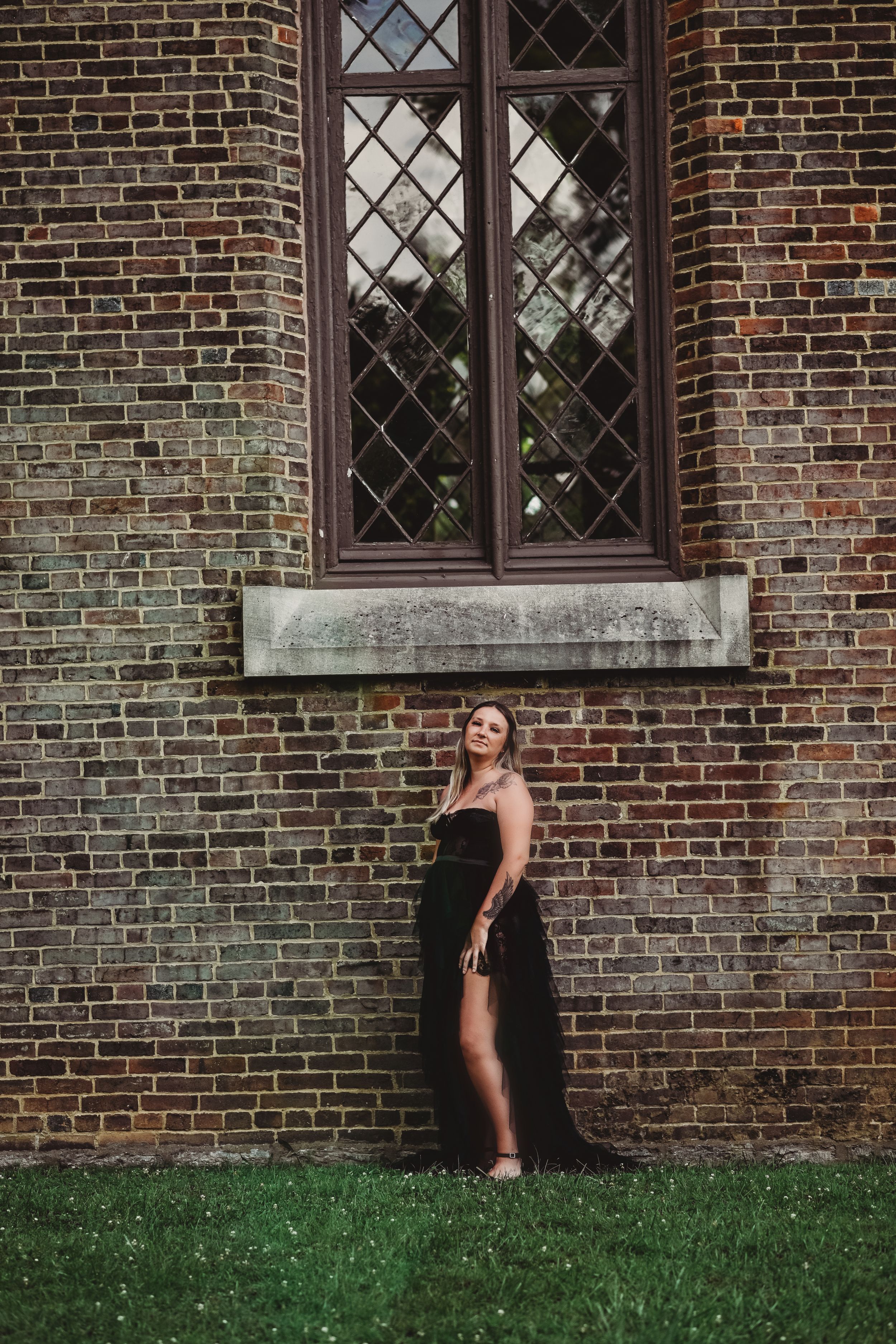 A black dress contrasts against a historic brick building with diamond-paned windows.