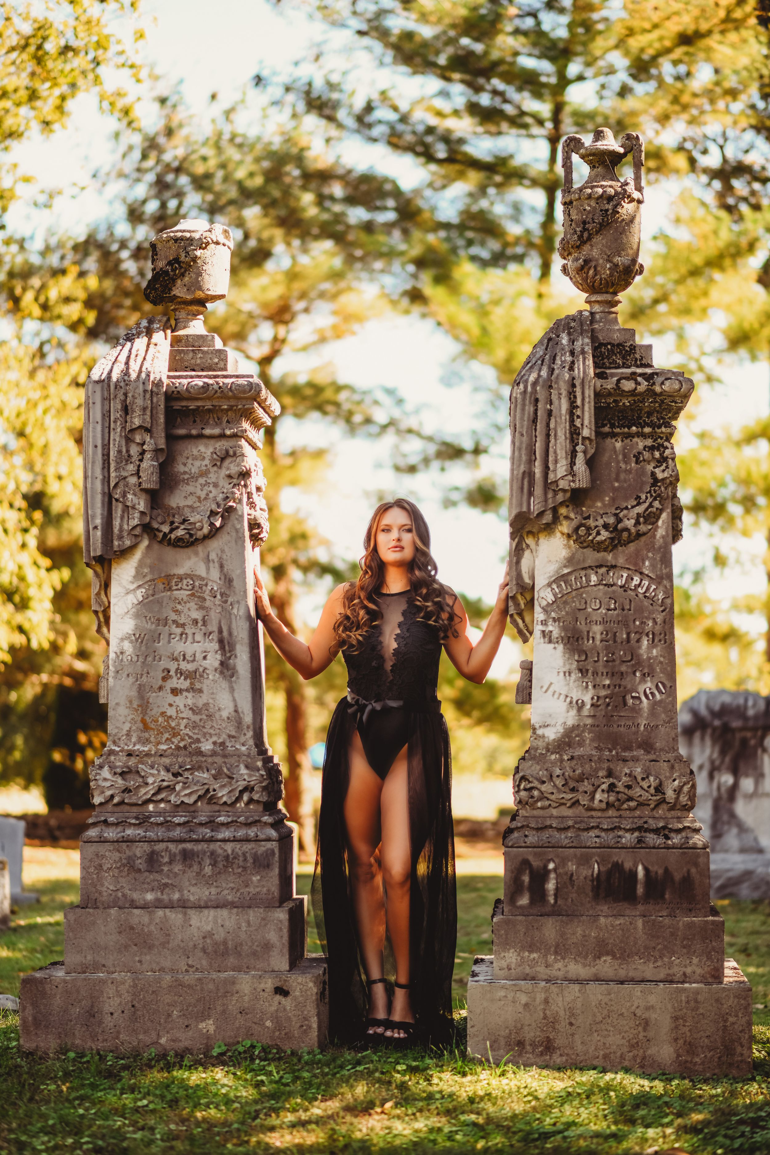 Dramatic portrait between two ornate cemetery pillars in black flowing dress.