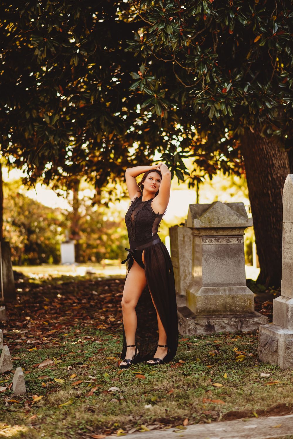 Autumn cemetery photoshoot with black dress against golden sunset light filtering through trees.
