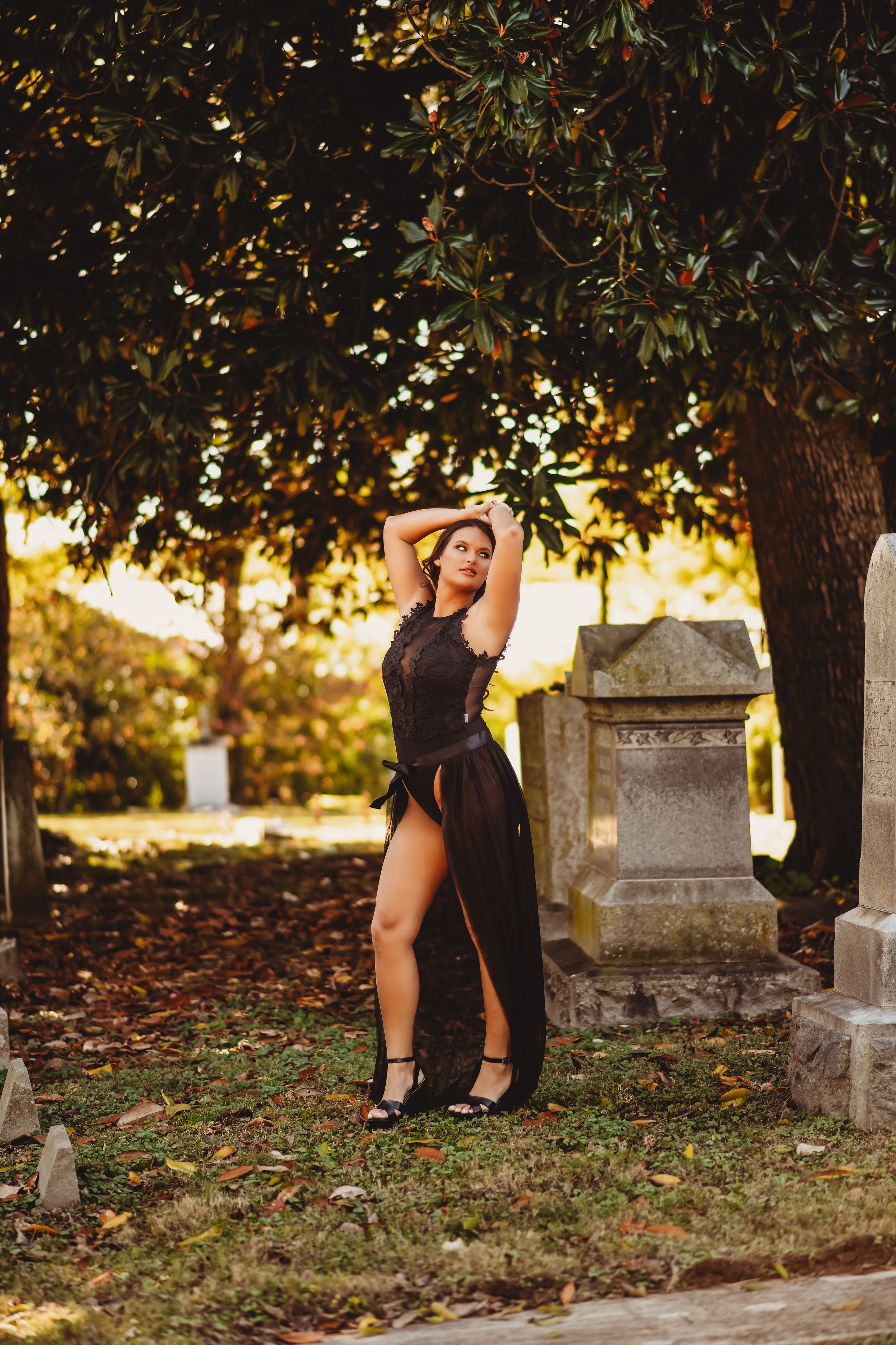 Autumn cemetery photoshoot with black dress against golden sunset light filtering through trees.
