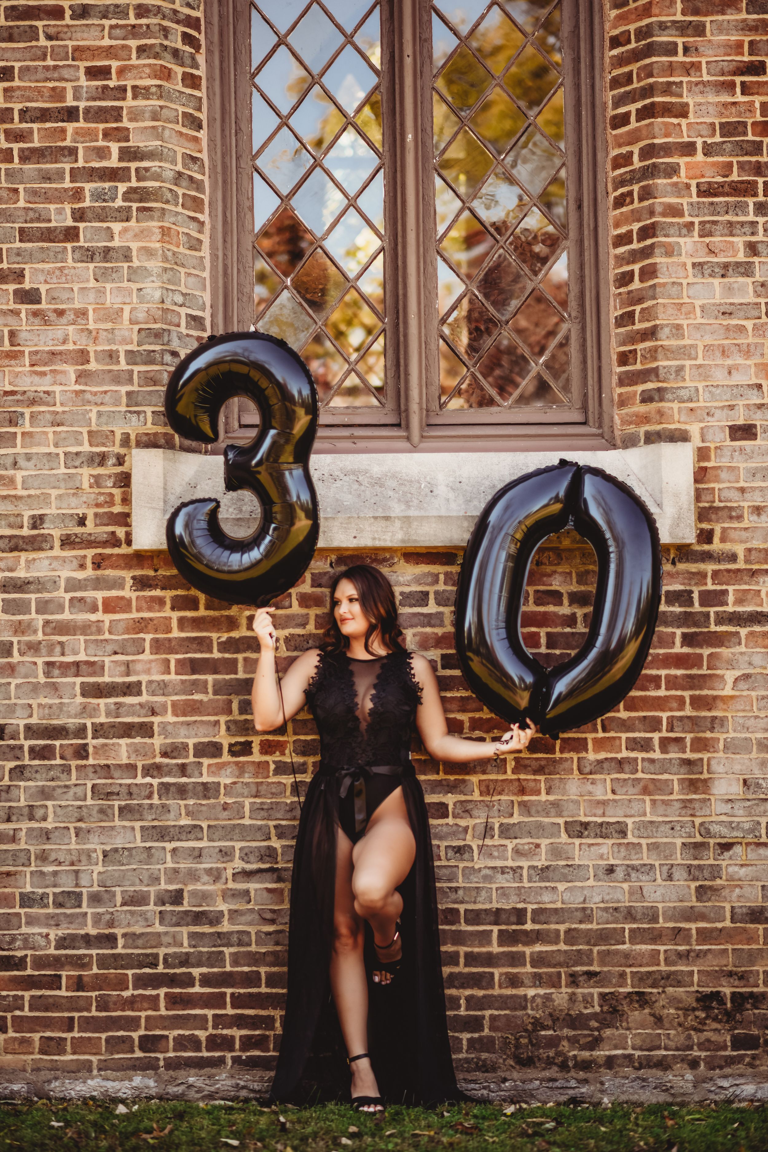 Black number balloons spelling 30 against brick church wall in artistic portrait.