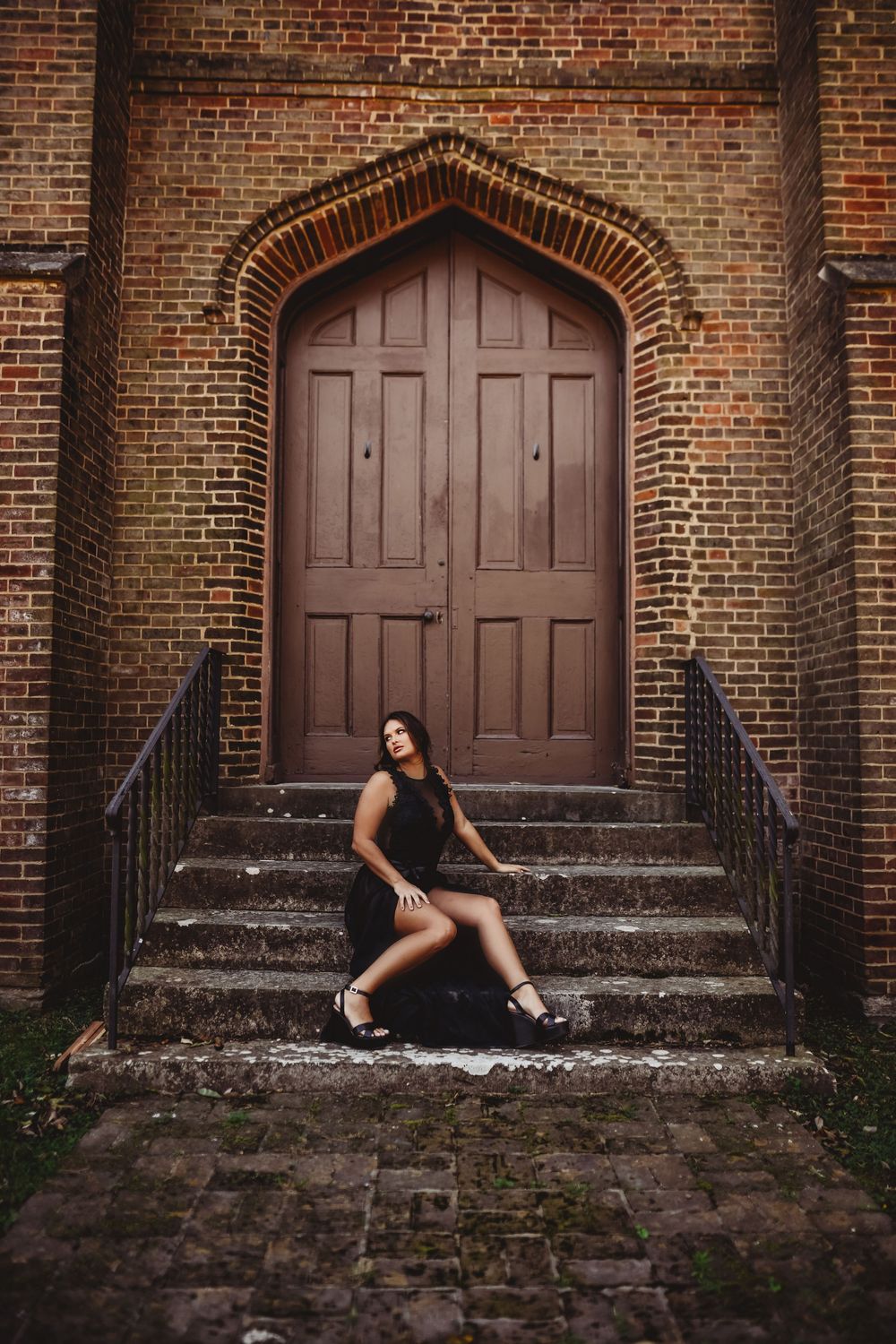Dramatic pose on church steps with gothic wooden door backdrop.