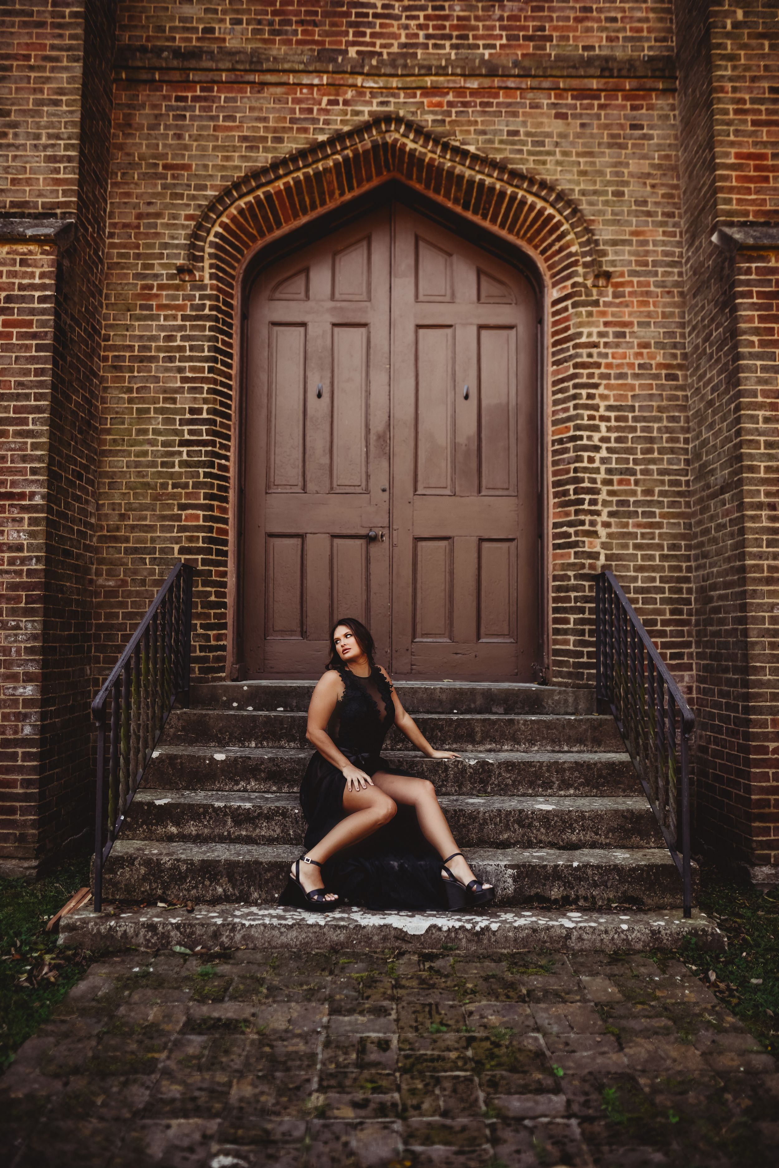 Dramatic pose on church steps with gothic wooden door backdrop.