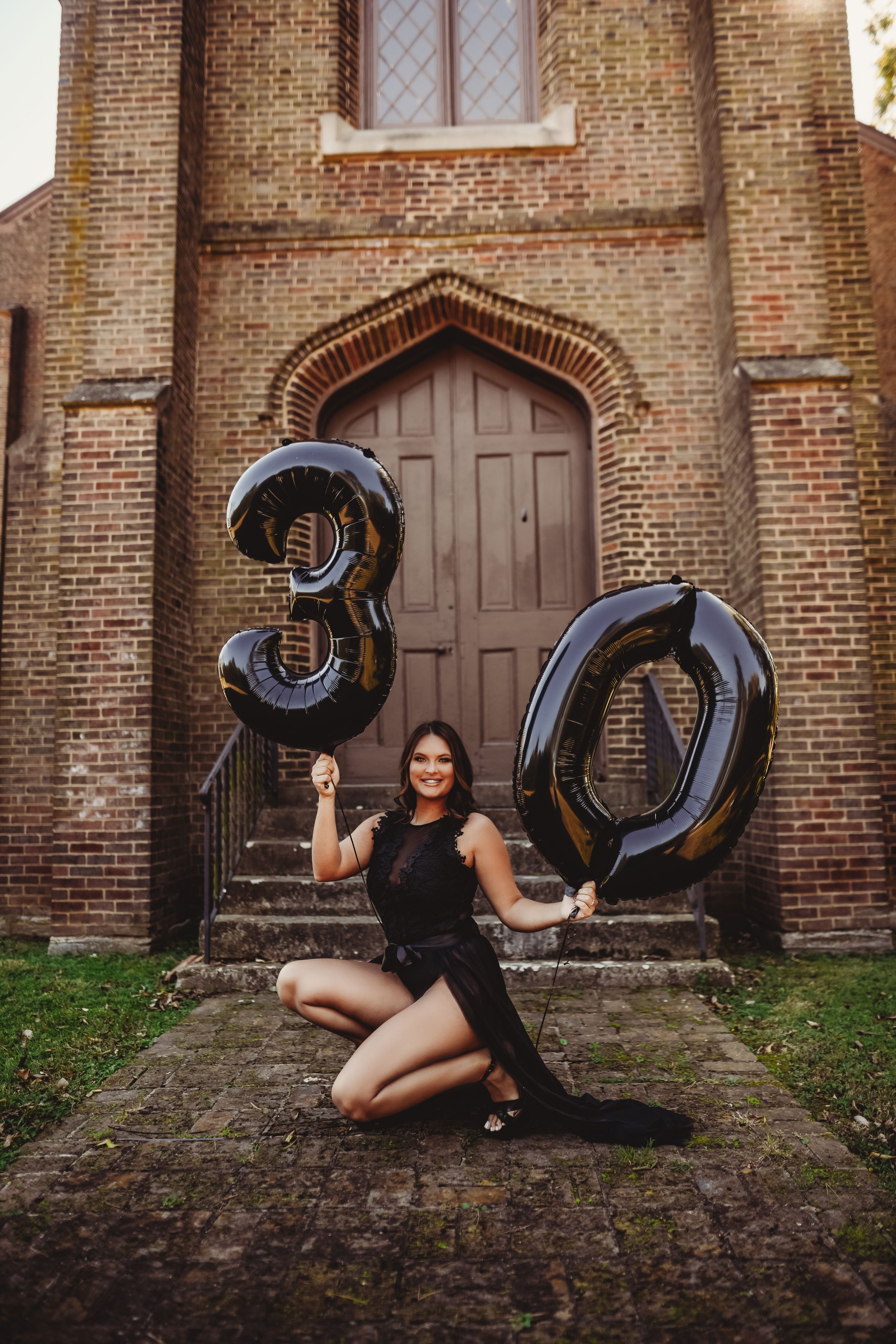 Birthday celebration portrait with black number 30 balloons on church steps.