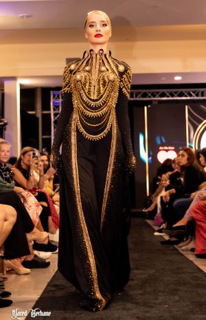 Elegant black gown with ornate gold chain details and high neckline displayed on fashion runway.