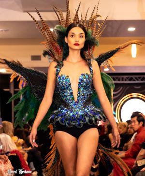 Glamorous blue sequined bodysuit with dramatic feather headdress and details shown on fashion runway.