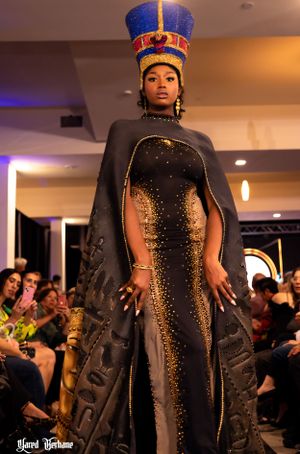 Elegant black gown with gold accents and dramatic Egyptian-style headdress shown at fashion event.