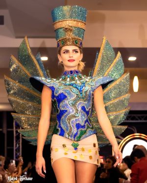 Futuristic aqua and blue costume with metallic winged headpiece and geometric patterns on runway.