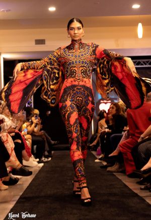 Fashion model walks runway in ornate red and black patterned jumpsuit with dramatic flowing sleeves at luxury fashion show.