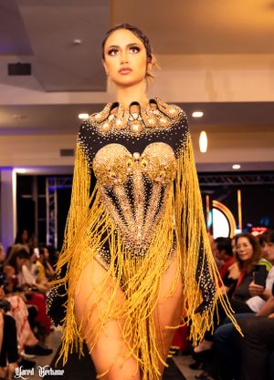 Glamorous gold fringe bodysuit with jeweled neckline sparkles on fashion runway against dark backdrop.