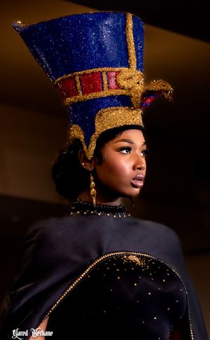 Fashion model wearing ornate Egyptian-inspired blue and gold headdress in dramatic lighting.