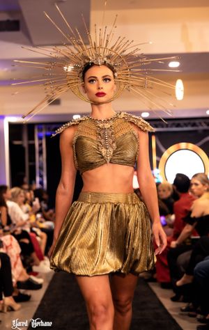 Model wears golden two-piece outfit with dramatic spiked crown headpiece on catwalk.