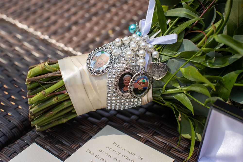 Bridal bouquet wrapped with pearl-adorned ribbon featuring memorial photo charms of loved ones.