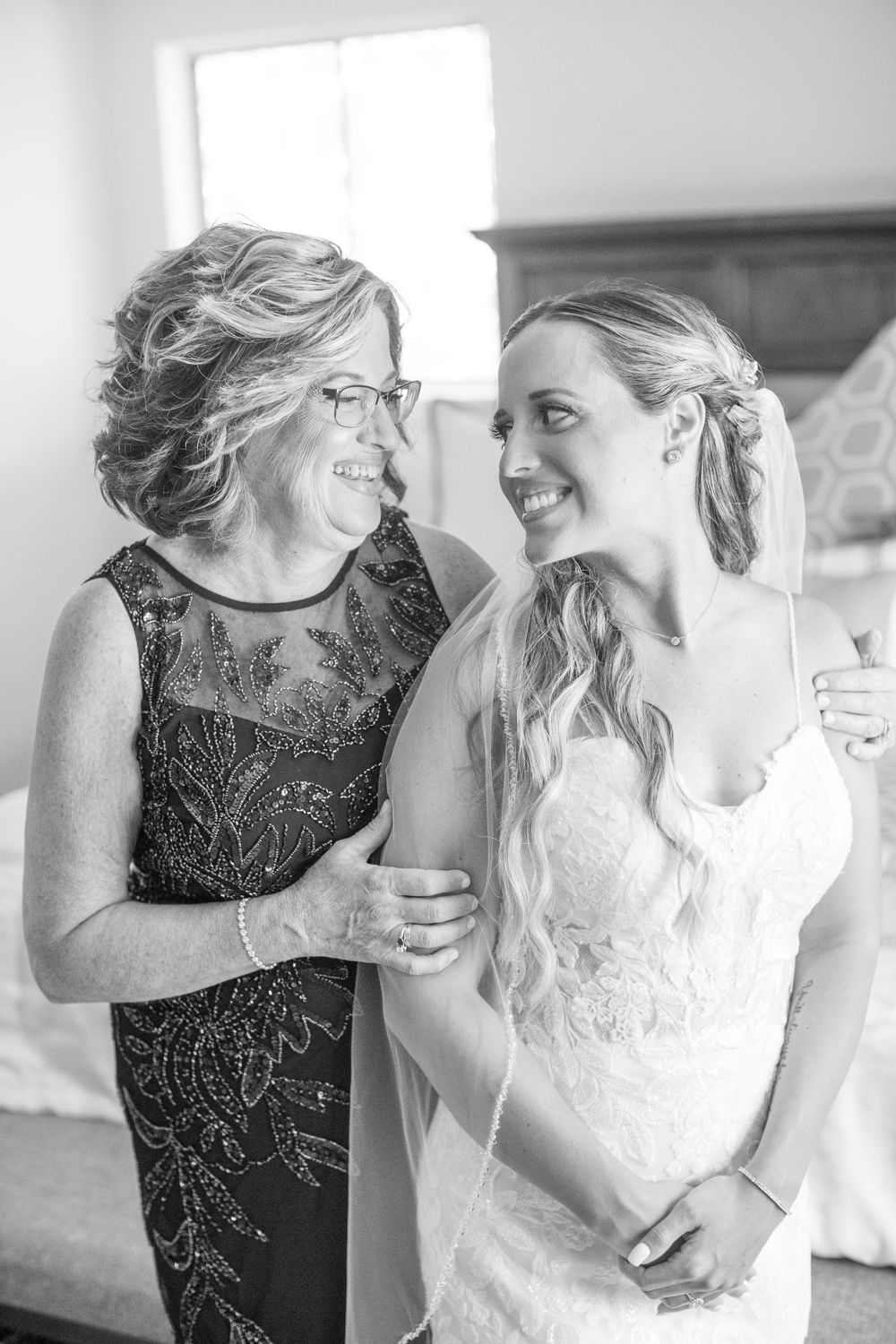 Black and white photo of smiling mother and bride in wedding dress sharing a joyful moment.