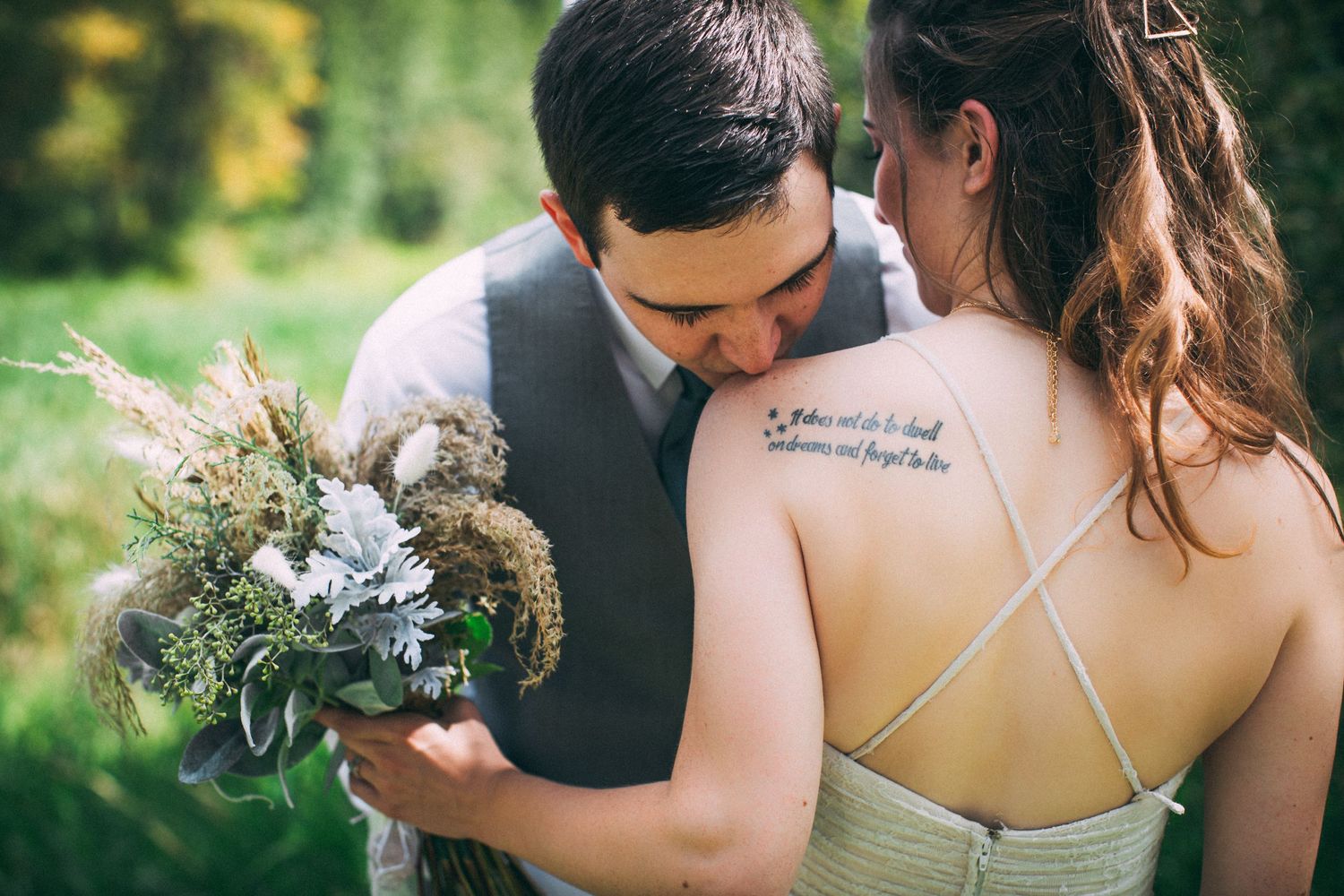 Wedding couple holds rustic wildflower bouquet against green outdoor setting.