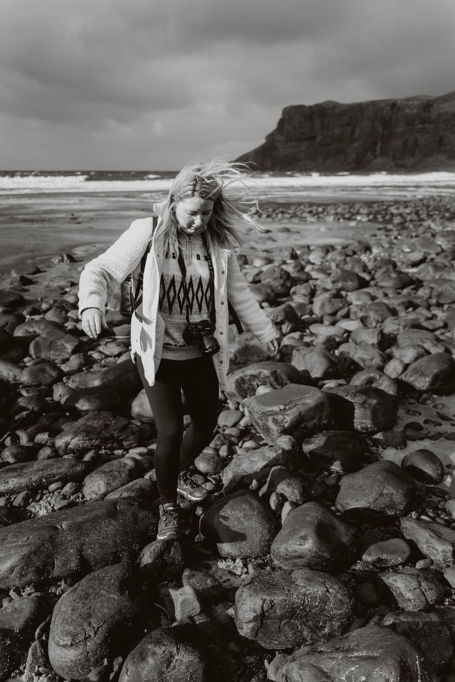 A dramatic black and white photo of someone traversing rocky coastal terrain.