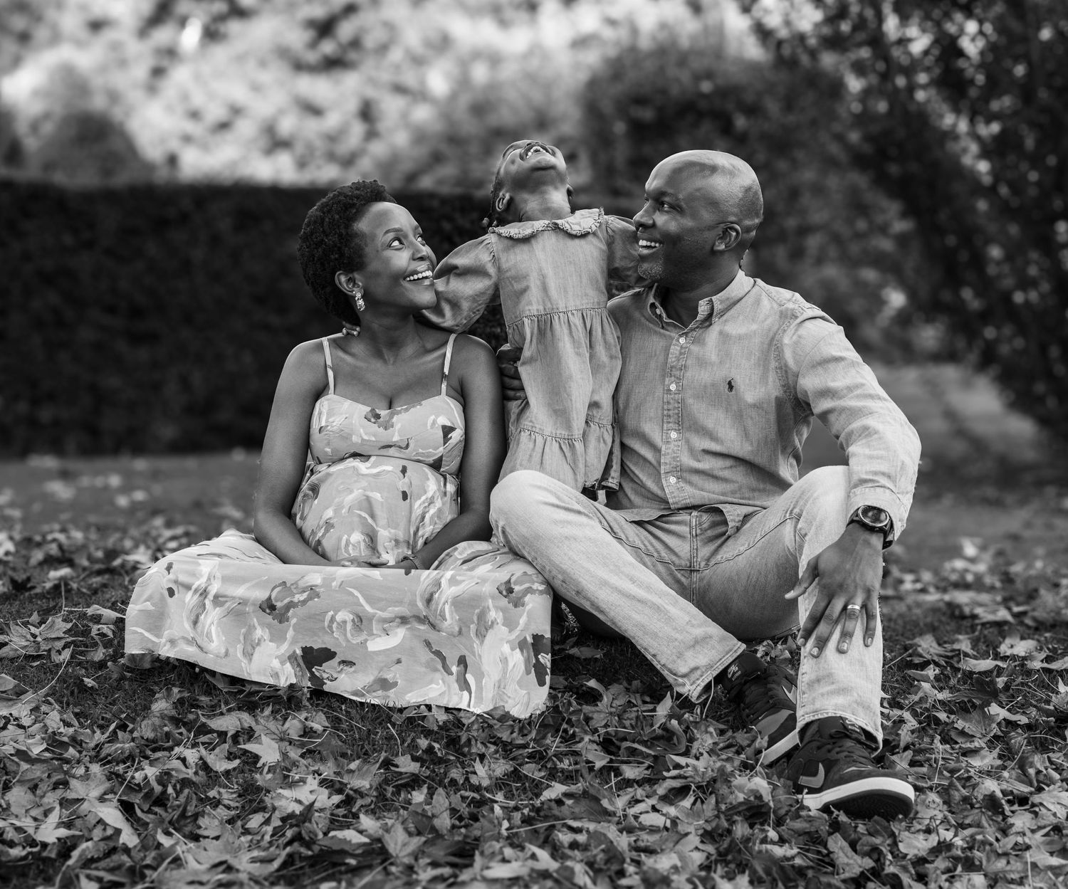 Black and white family portrait of three people sitting together outdoors on grass.