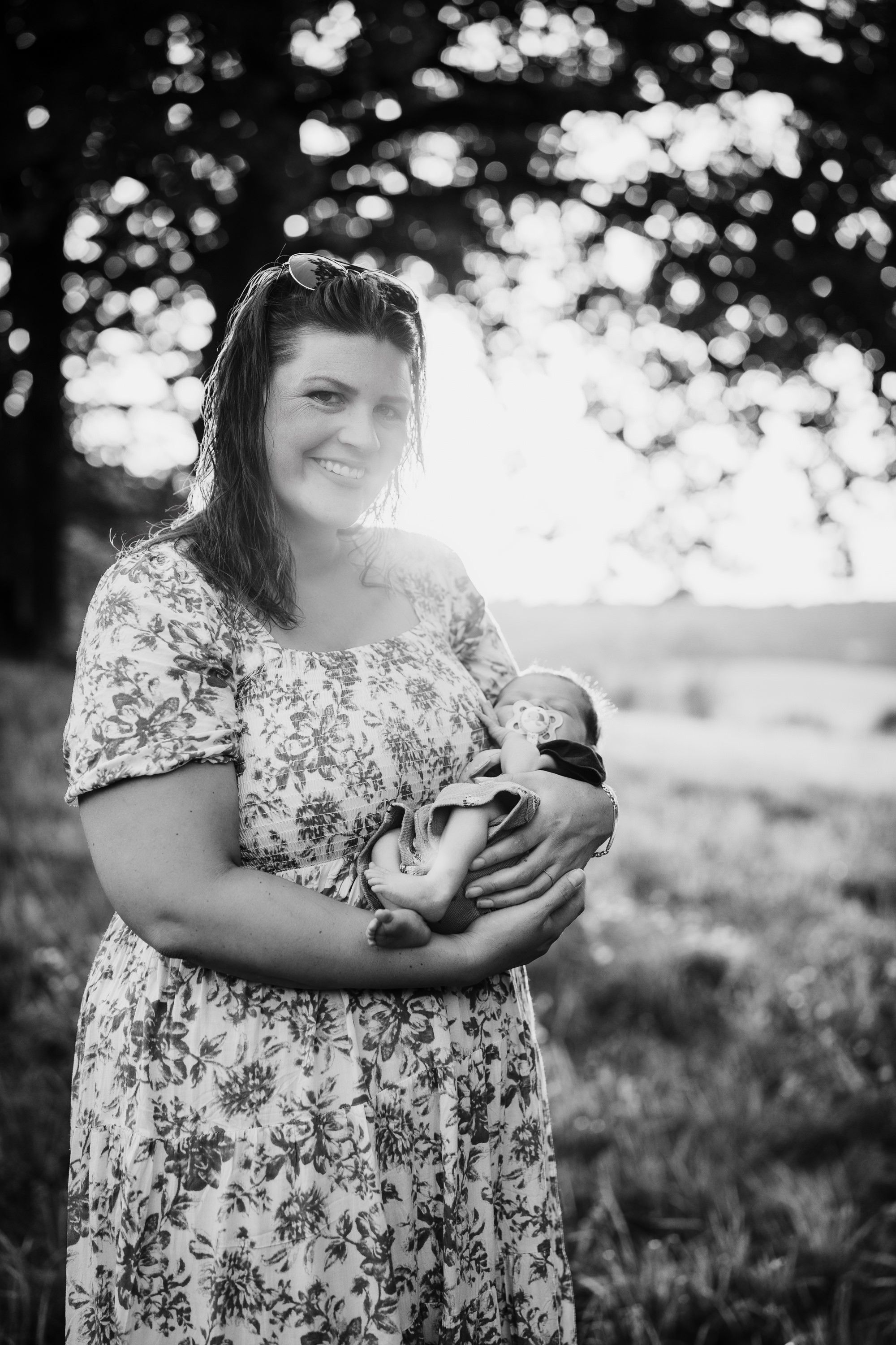 Black and white candid portraits showing tender moments between a mother and baby in a natural outdoor setting.