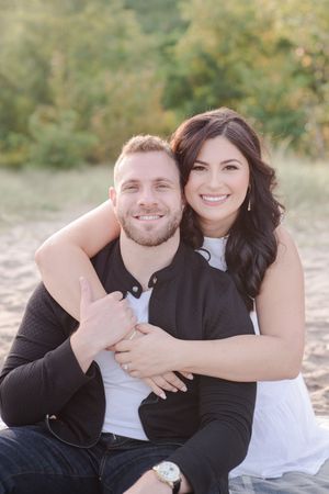 Happy couple embracing and smiling together while sitting on a sandy beach outdoors.