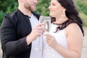 Couple clinking champagne glasses together and smiling during an outdoor engagement session.