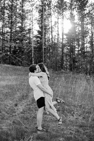 Black and white photo of man lifting woman in a loving embrace in a sunlit forest meadow.