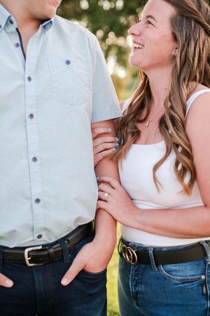 Woman laughing and holding mans arm outdoors, showing off diamond engagement ring in golden light.