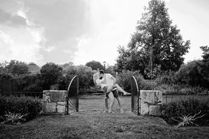Black and white photo of couple sharing a dramatic dip kiss between stone garden gate pillars.