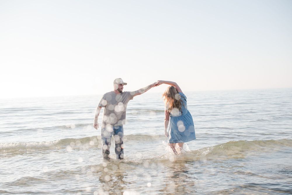Couple dancing playfully in ocean waves on a bright sunny beach day.