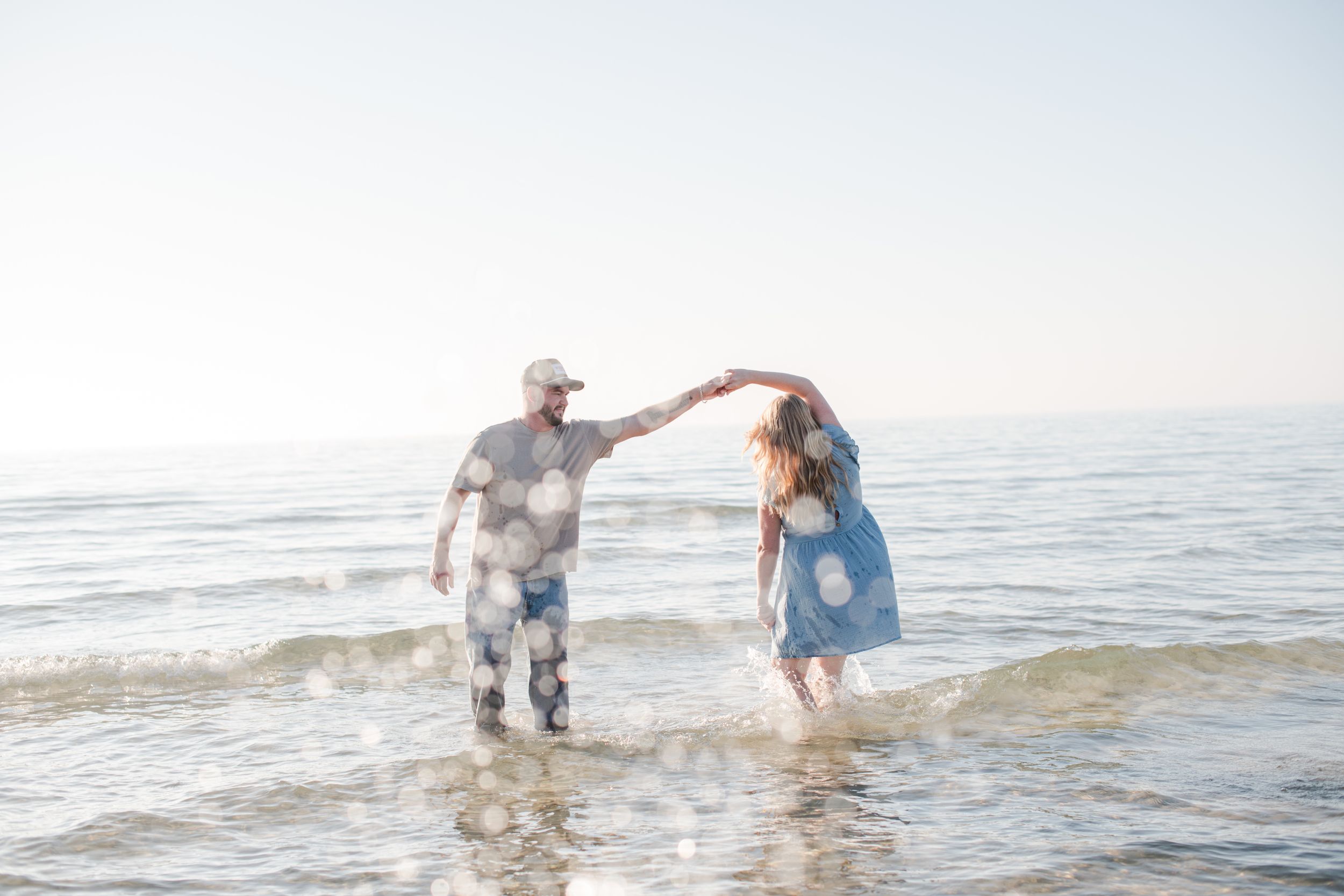 Couple dancing playfully in ocean waves on a bright sunny beach day.