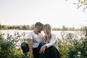 Couple sitting close together touching foreheads romantically by a sunlit lake.