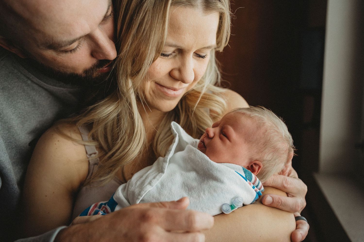 Parents share intimate moment with newborn baby in hospital room.