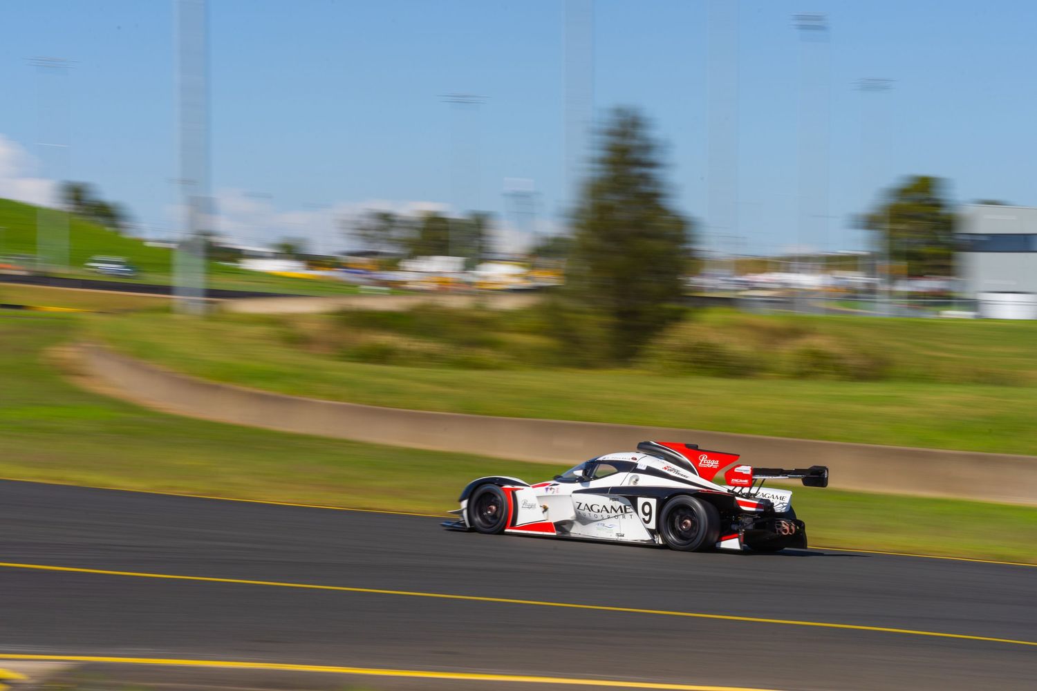 Race car speeds along track with rolling hills in background.