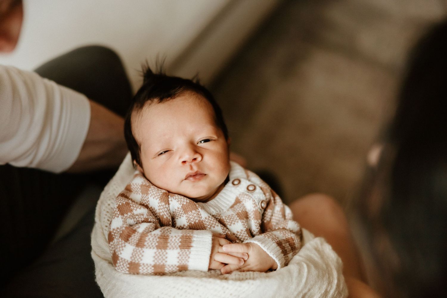A small baby in a brown checkered outfit lays comfortably swaddled and wrapped in a white blanket.