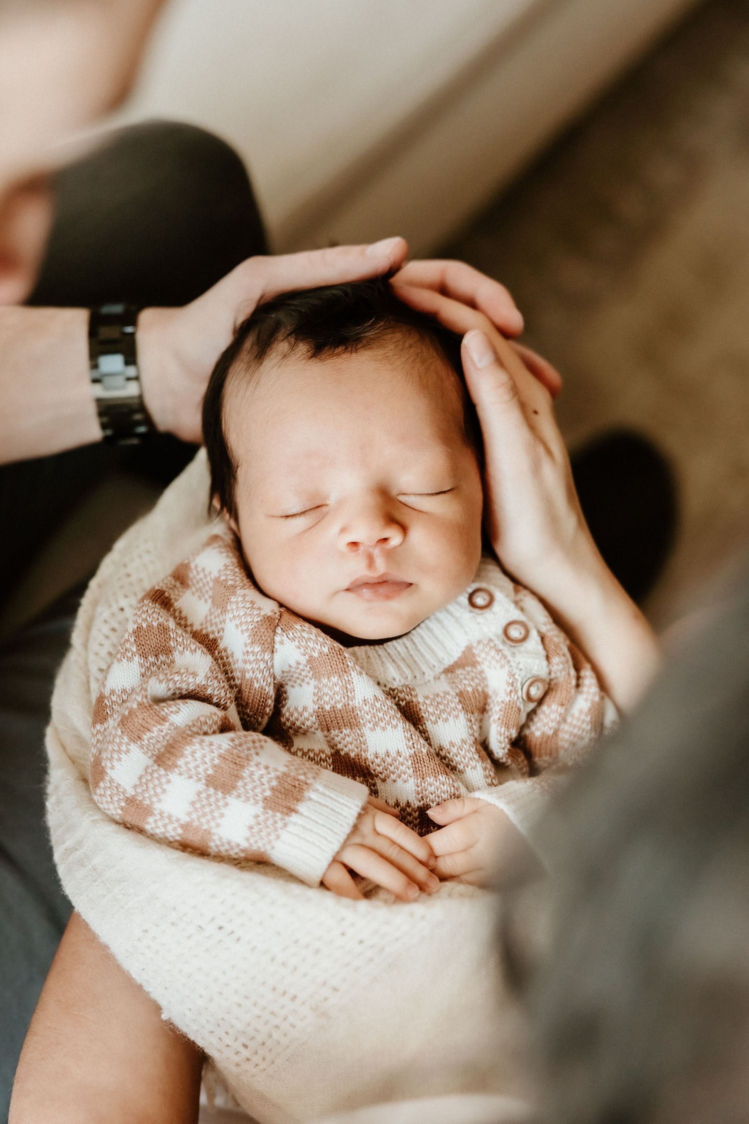 A sleeping newborn baby wearing a checkered sweater rests peacefully in a caregiver's gentle embrace.