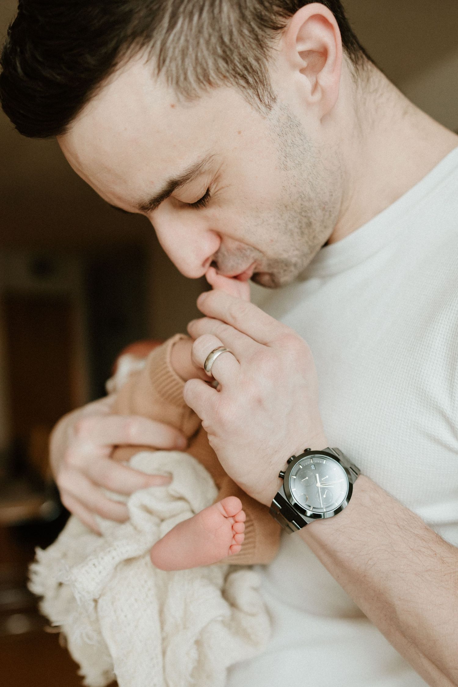 A tender parental moment showing someone gently kissing a tiny baby's foot while wearing a white shirt and wristwatch.