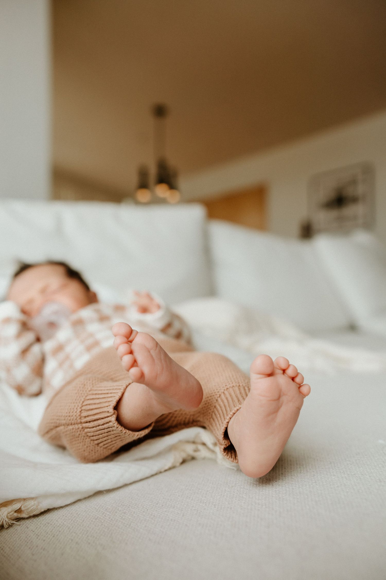 Small bare baby feet peeking out from a knit blanket while resting on white couch cushions.